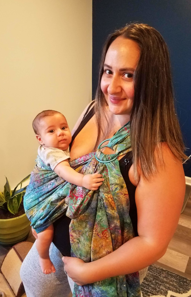 Mother carrying baby in a sling style carrier.