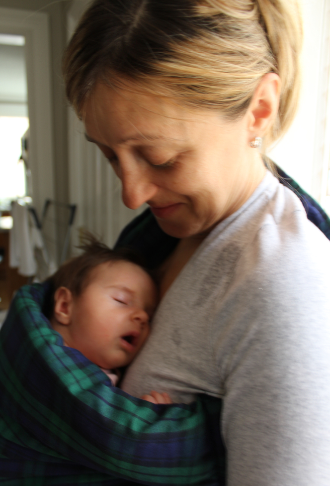 Mother holding baby in a sling style carrier.